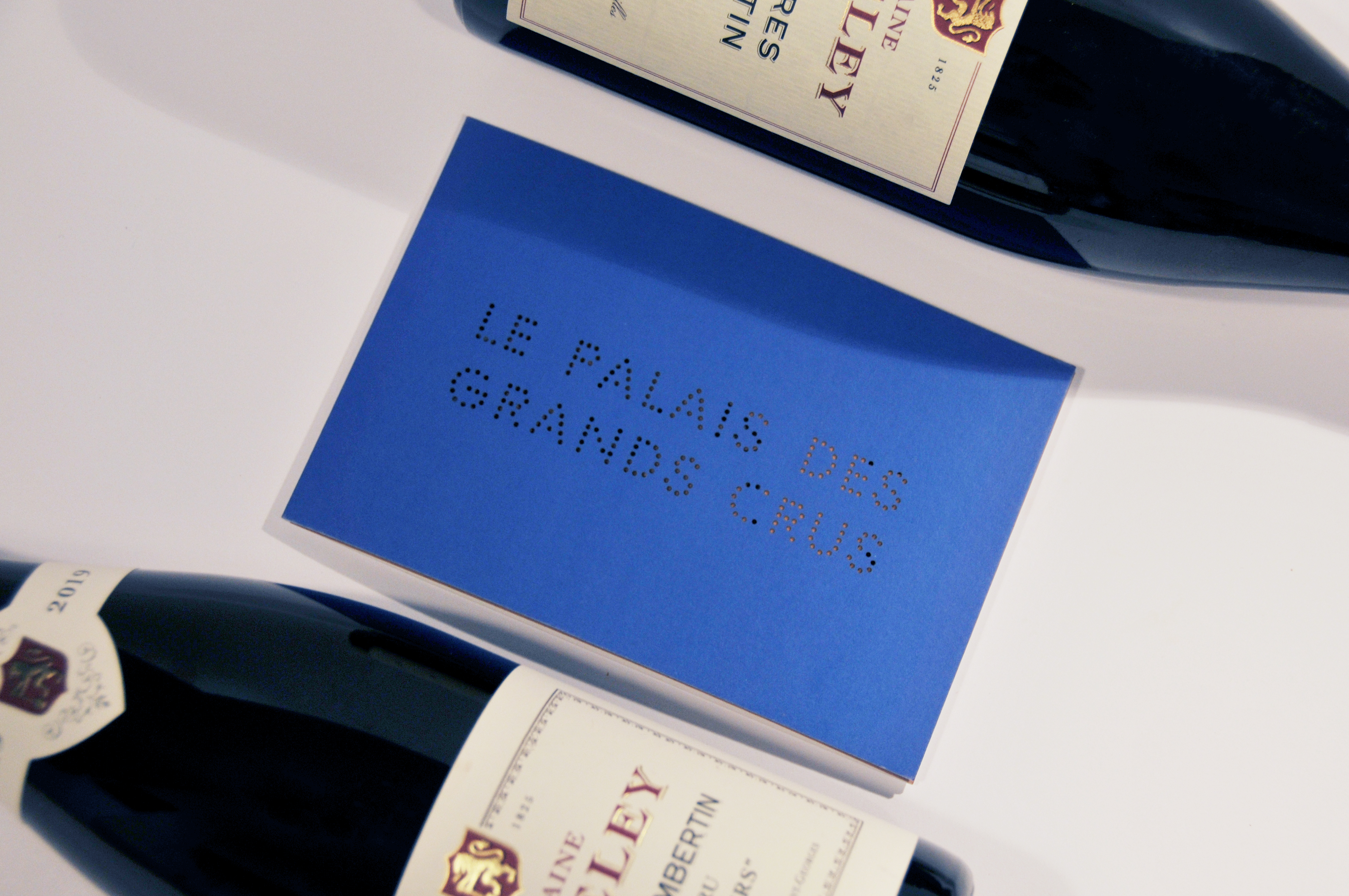 Blue Palais des Grands Crus wine programme photographed between fine-wine bottles